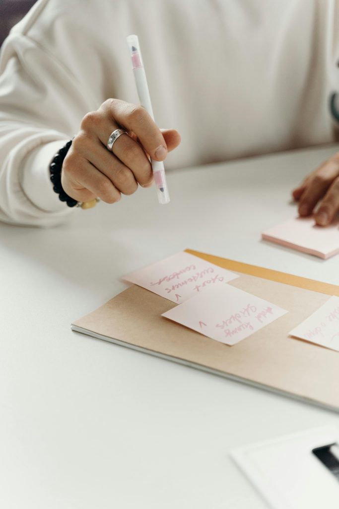 Close-up shot of a hand writing with a pen on pink sticky notes placed on a desk.
